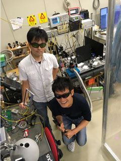 実験装置をバックにレーザー保護眼鏡をかけた状態でのスナップショット（武田：左、宇佐見：右）