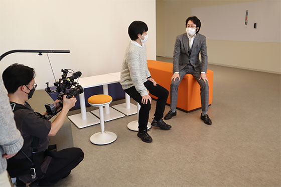 学生さんとの会話シーンでは、カメラマンの背中からのびる支えを使った手持ちカメラで撮影。学生さんもちょっと緊張気味?